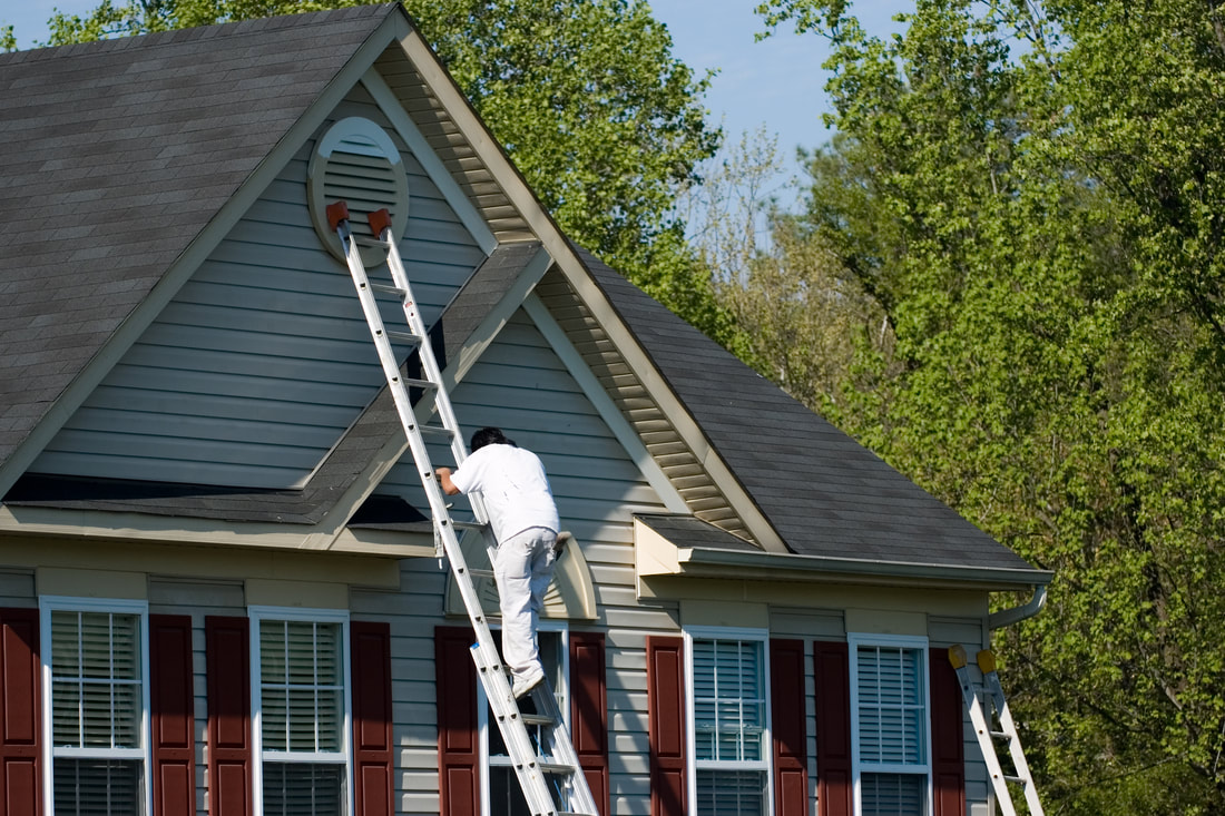 Man on ladder painting siding of house